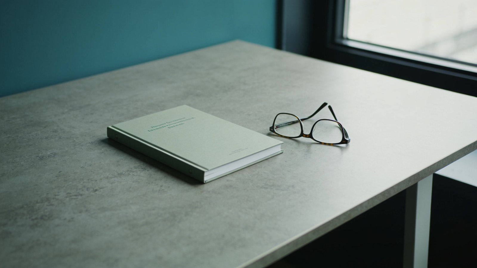 A single slim report and reading glasses on an empty table